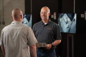LaserCraft leadership team member talks to laserCraft employee while holding metal part