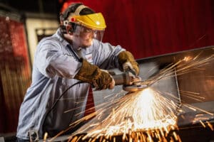 Man in protective gear grinds a piece of metal