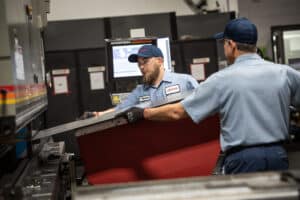 Two lasercraft employees load piece of metal into machine