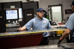 Laser Craft Tech employees load a piece of metal into a fabrication machine