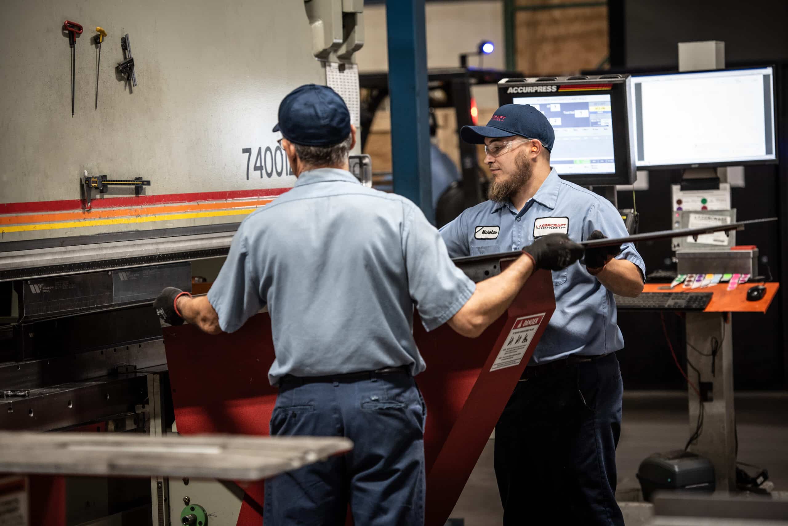 Laser Craft Tech employees load a piece of metal into a fabrication device