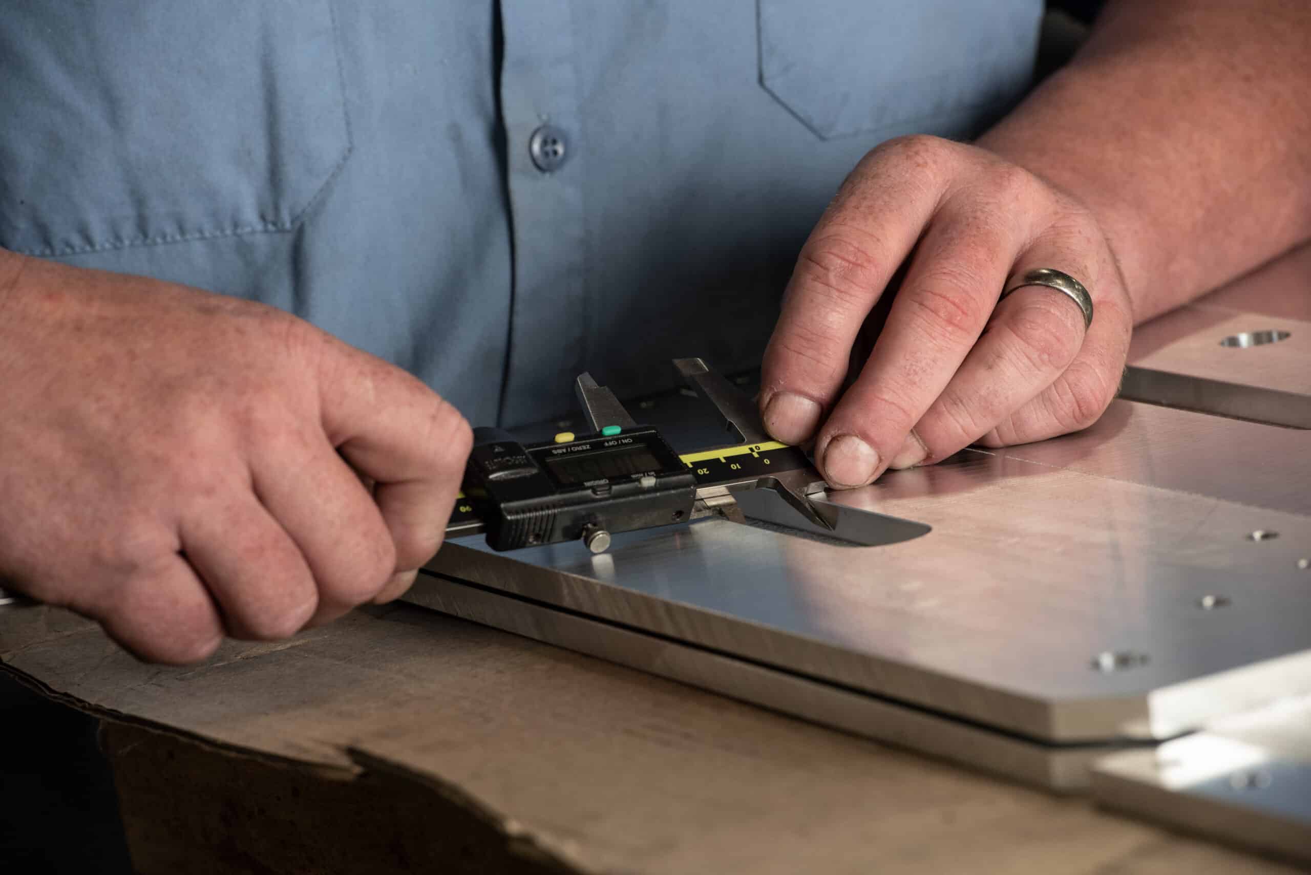 Laser Craft Tech employee checks a piece of metal with a caliper